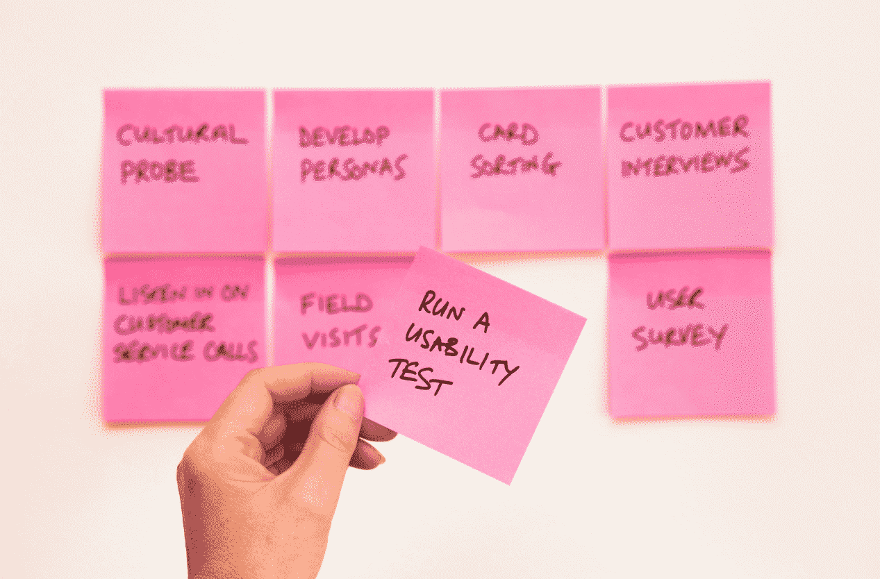 A hand holding up a pink post it that says run a usability test