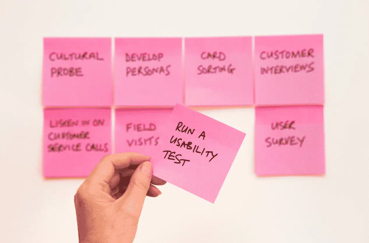 A hand holding up a pink post it that says run a usability test