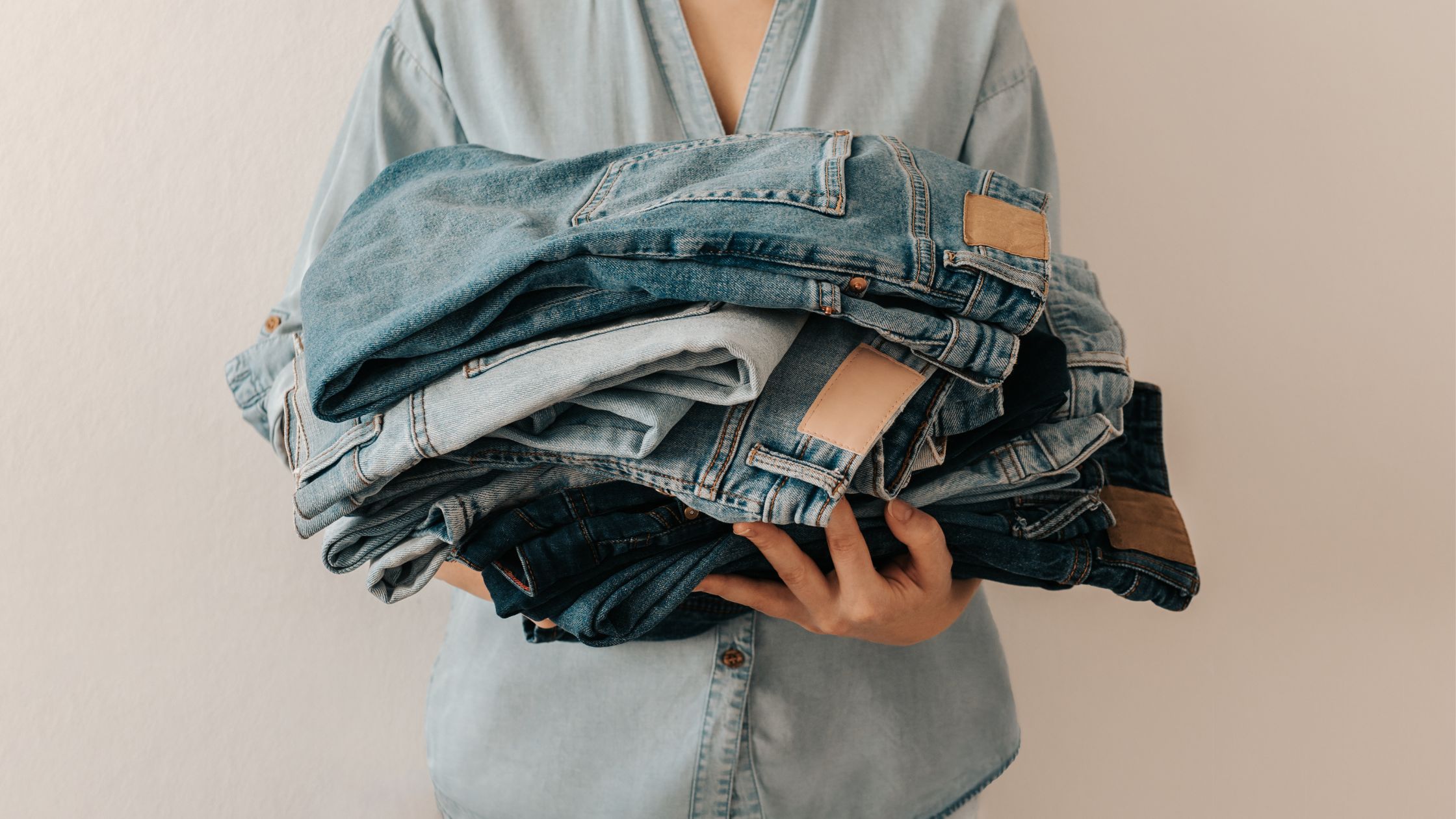 a girl holding a pile of folded jeans in front of her